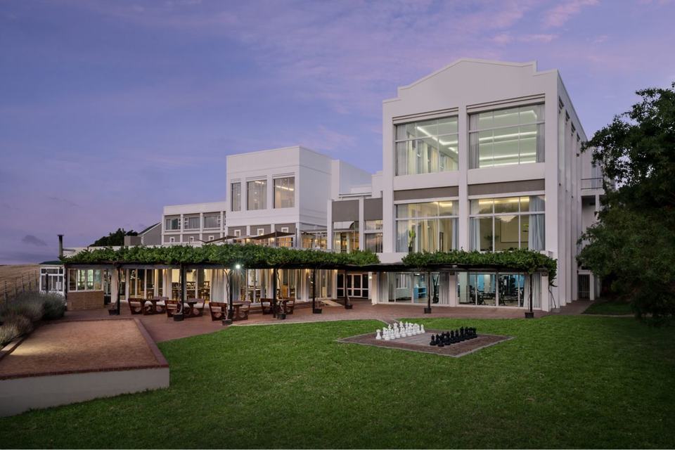 The Protea Hotel Stellenbosch Technopark at dusk, with its lawn and outdoor chess set.