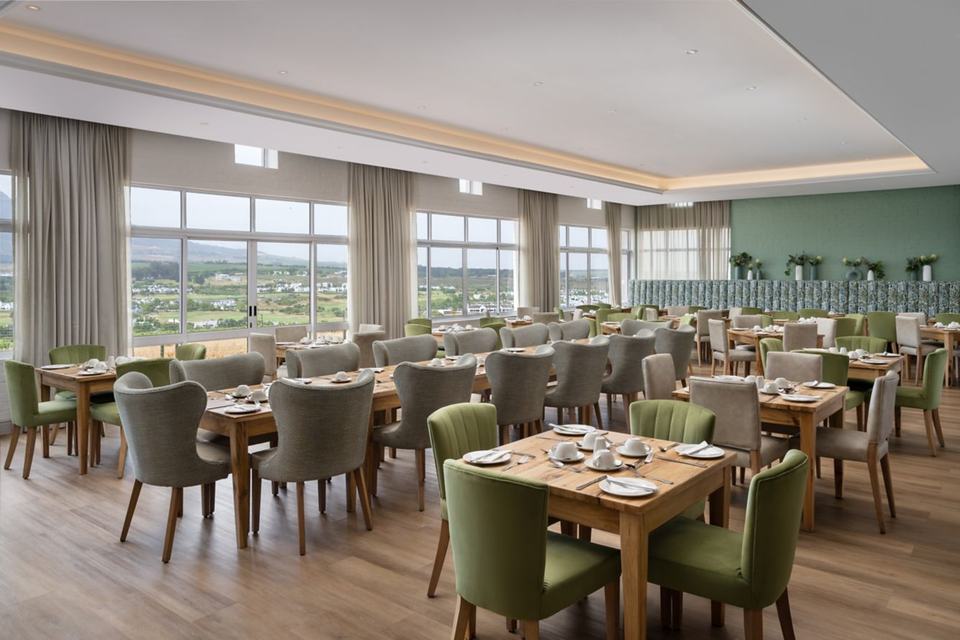 The hotel restaurant, with green chairs and wide windows.