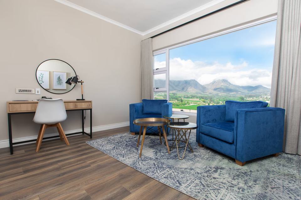 A room with a desk and two blue armchairs by a window onto the mountains.